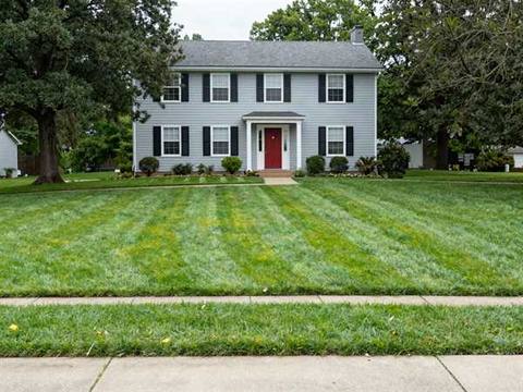 The same front lawn cut short and evenly, with mower stripes running across it and a clean edge along the sidewalk.