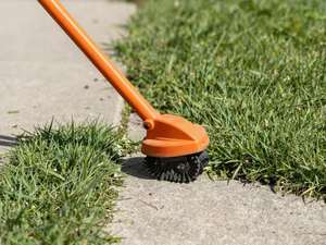 An orange string trimmer cutting the grass back to a hard line along the edge of a concrete walkway.