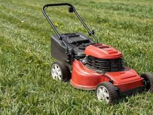 A red push mower standing on a half-cut lawn, the mown strip clearly lighter than the grass beside it.